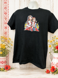 A beautiful short-sleeved shirt featuring a design of a mother with her daughter standing by her legs; both are wearing red shoes.